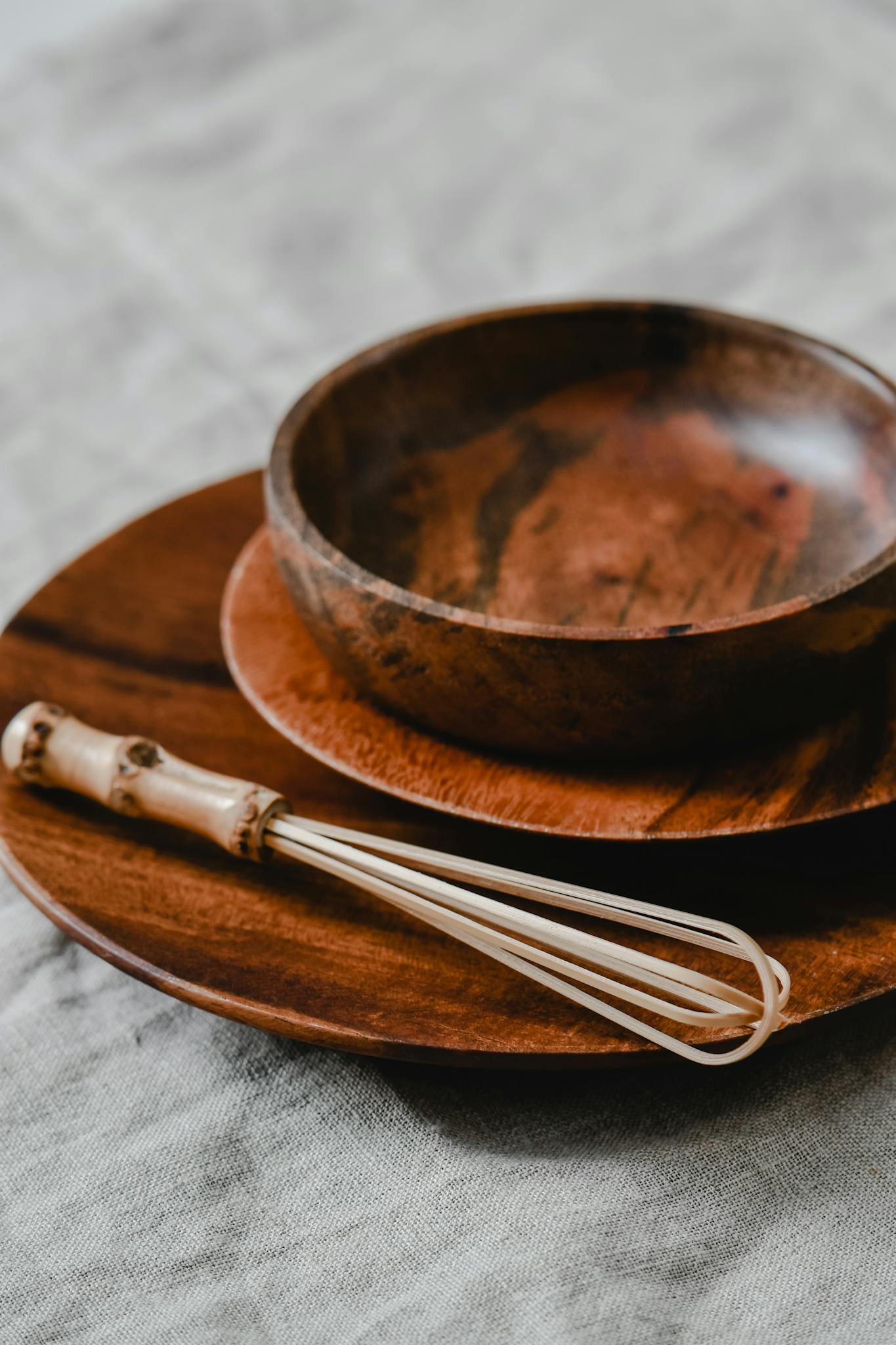 A close-up of rustic wooden bowls and plates with a whisk on a textured surface, perfect for kitchen-themed designs.
