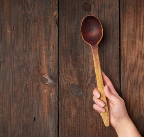 Hand holds an old brown wooden spoon, place for text